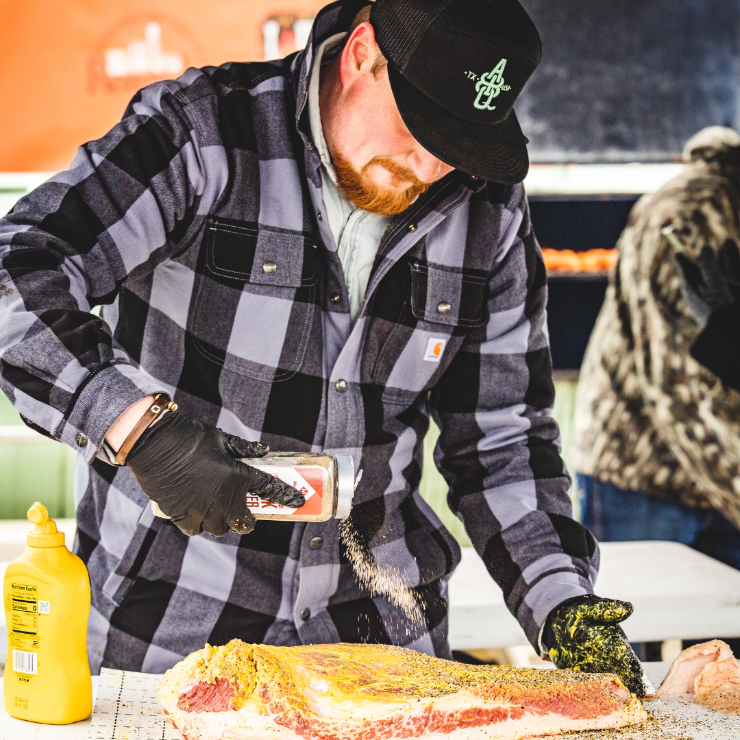 Male standing up sprinkling seasoning on a large piece of beef meat.